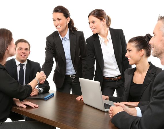 Business professionals in formal attire having a meeting and shaking hands around a table with a laptop