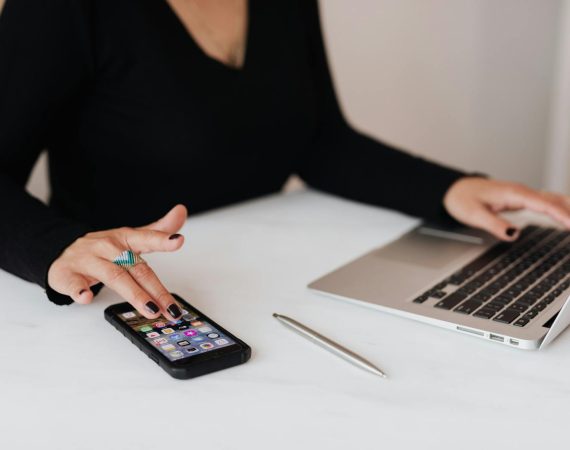 Crop woman using smartphone and laptop during work in office