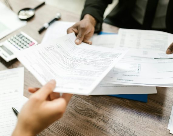 Business meeting with hands exchanging documents over a desk with papers, pen, and calculator visible