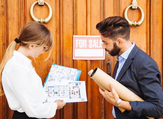 Real estate agents discussing property blueprints outside a house with a For Sale sign on wooden doors