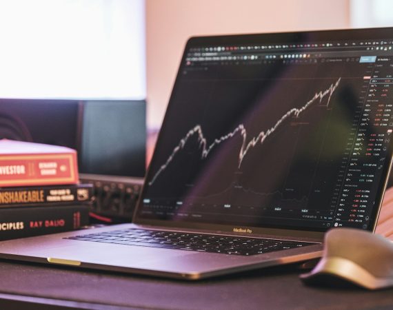 Laptop displaying stock market chart alongside investment books on a desk