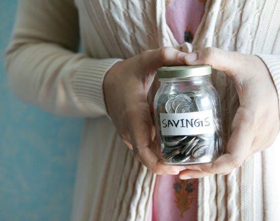 Person holding a savings jar filled with coins, promoting budgeting and financial planning strategies