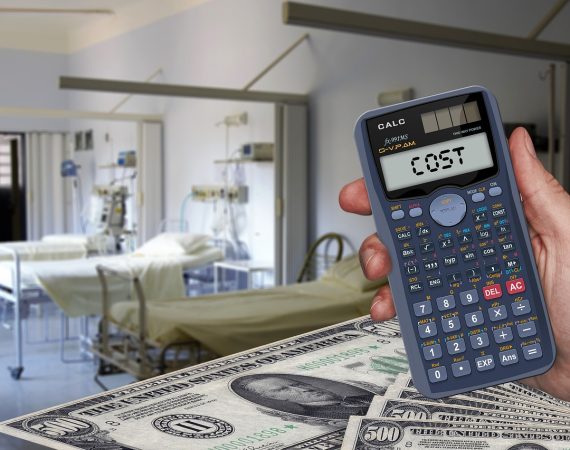 Calculator displaying cost with hospital beds and dollar bills in the background symbolising healthcare expenses