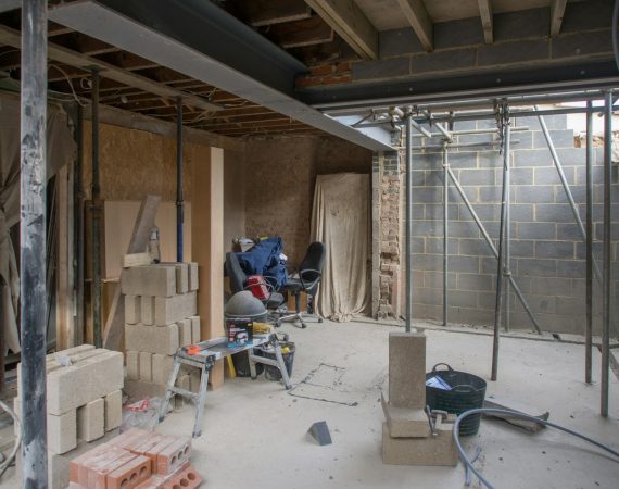 Building renovation site with tools, brick stacks, and scaffolding showing construction progress indoors