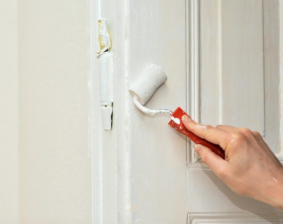 A person applies red paint to a white door using a brush, showcasing a creative home improvement project