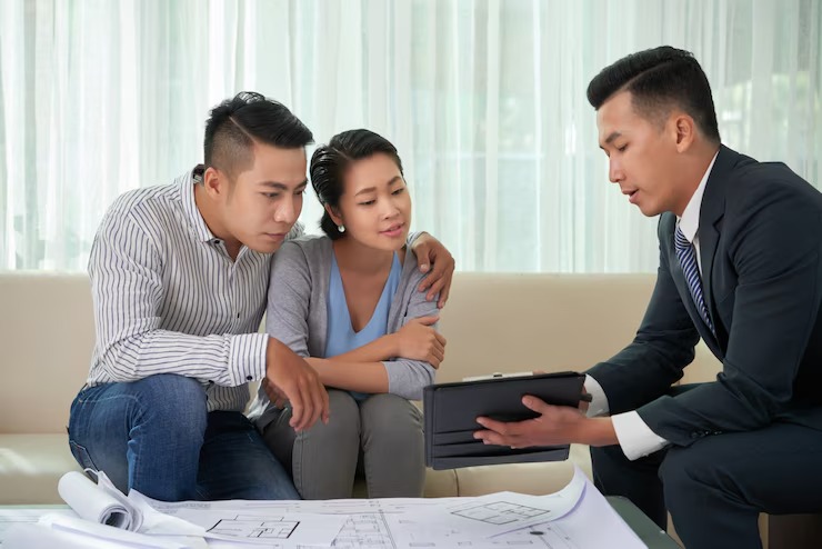 Couple consulting with financial advisor on house plans, seated on sofa, reviewing documents with a tablet at home