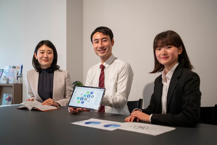 Three professionals in a meeting room with a tablet displaying charts, engaging in a business discussion