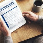 Person reviewing life insurance policy on tablet with coffee on wooden table