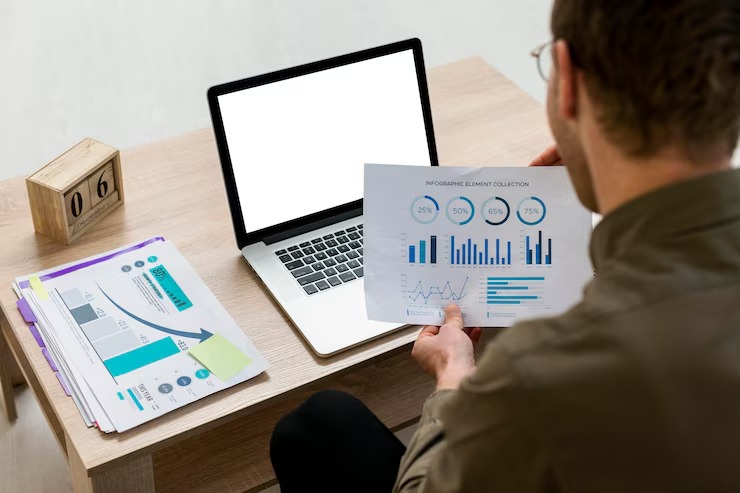 Person analysing financial graphs at desk with laptop and documents