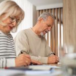 Elderly couple engaged in writing activities at home office setting