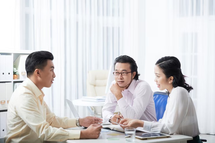Three colleagues having a discussion at a modern office table with documents and laptops