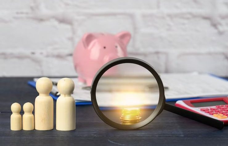 Wooden figures with magnifying glass on coins, piggy bank, and calculator symbolising family budgeting and savings