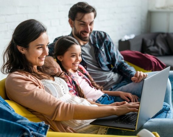 A family of four sitting together on a couch, using a laptop for a shared activity
