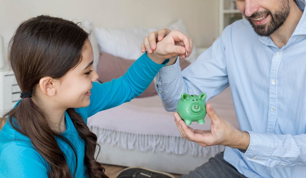 A man and a little girl are smiling as they hold a colorful piggy bank, representing their shared savings goal