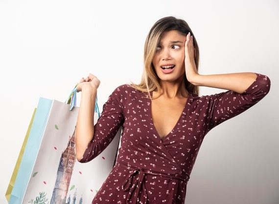 A surprised woman holds several shopping bags, her eyes wide with astonishment at her recent purchases