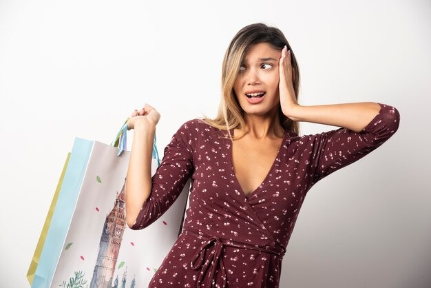 A surprised woman holds several shopping bags, her eyes wide with astonishment at her recent purchases