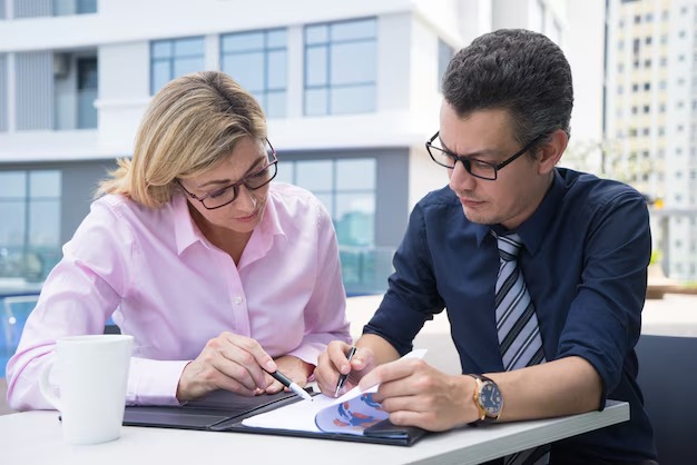 Businessman and woman collaborating on a business plan at a table with documents and a laptop