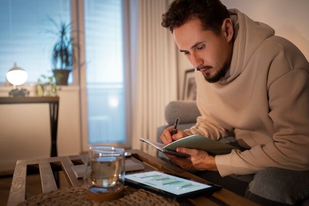 A man sits on a couch, focused on writing in a notebook with a pen in hand