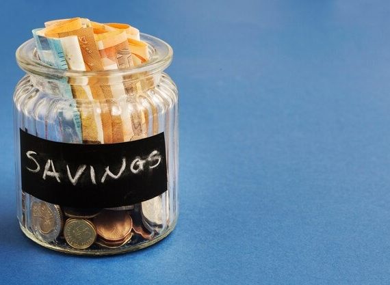 A clear savings jar filled with various coins and bills, symbolizing financial savings and budgeting