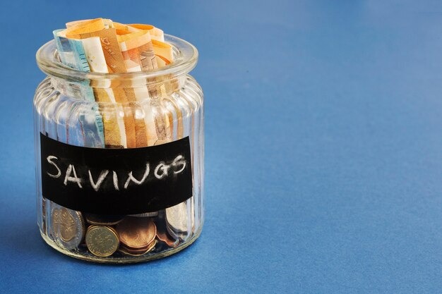 A clear savings jar filled with various coins and bills, symbolizing financial savings and budgeting