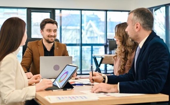 Four business professionals seated at a table, each using a laptop for a collaborative meeting