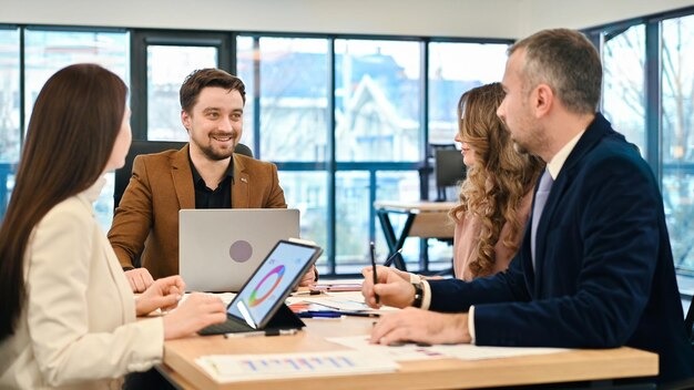 Four business professionals seated at a table, each using a laptop for a collaborative meeting