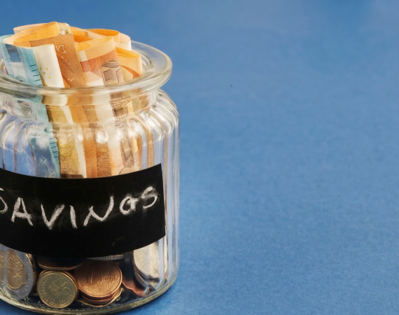 Jar filled with euro banknotes and coins labeled 'savings' on blue background